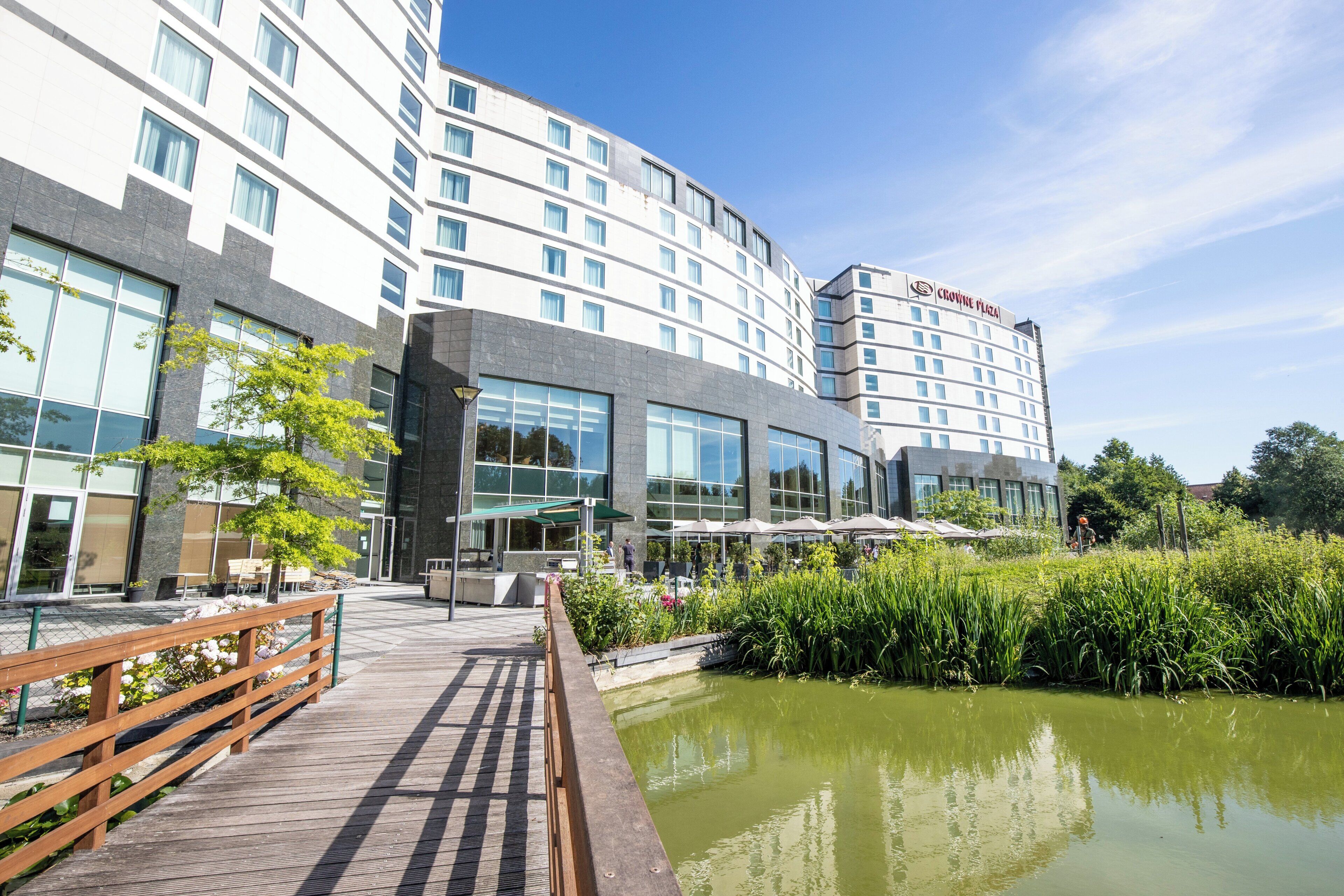 Un hotel moderno con fachada de vidrio, asientos al aire libre y una fuente de agua.