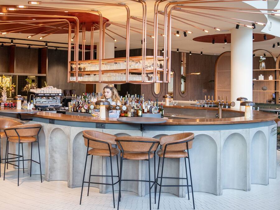 A modern bar area with a bar counter, stools, and a variety of bottles and glasses.
