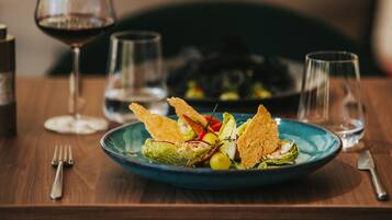 A plate of food on a wooden table with a wine glass and a bottle in the background.