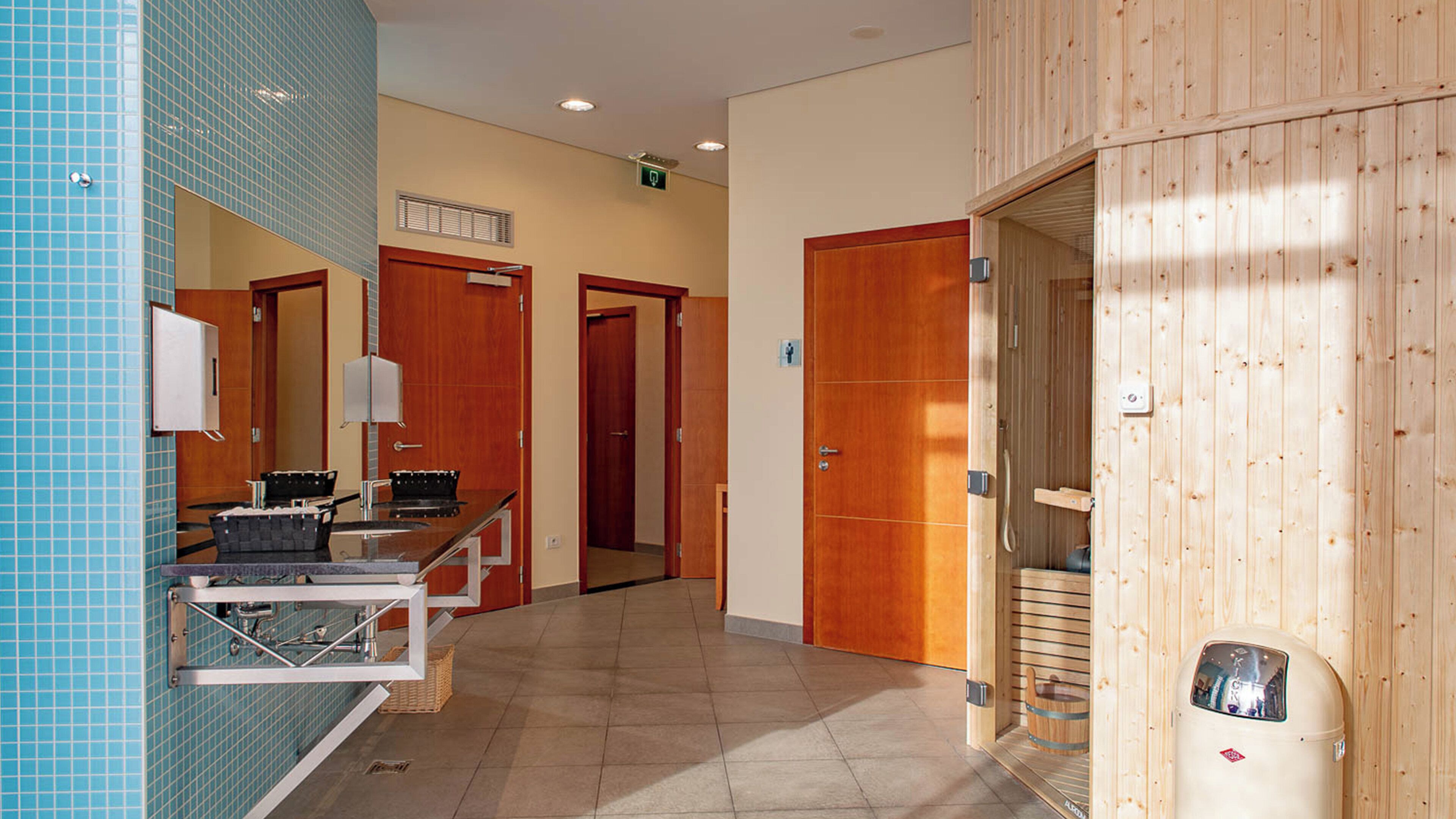 Un hall de hotel con mostrador de recepción, un espejo, una sauna de madera y una pared de azulejos.