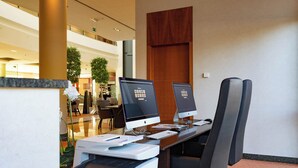 A hotel reception area with two Apple iMac computers on desks, a printer, and a seating area with chairs. - Crowne Plaza Brussels Airport by IHG (Machelen)