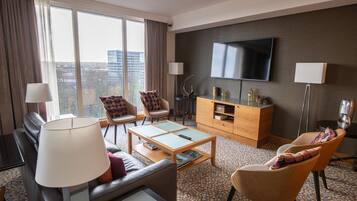 Habitación de hotel con sofá, sillones, mesa de centro, televisor y mueble.