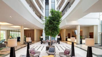 A spacious lobby with a central seating area, multiple floors, and a large tree.