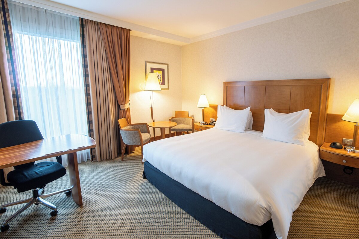 Ein Hotelzimmer mit einem großen Bett, einem Schreibtisch, einem Stuhl, einem kleinen Tisch und zwei Lampen.