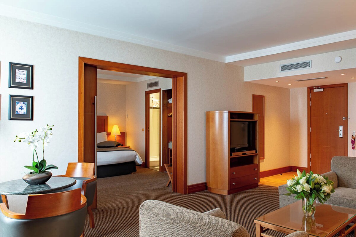 Ein Hotelzimmer mit Bett, Fernseher, einer Kaffeemaschine und einer Sitzecke mit Tisch und Stühlen.