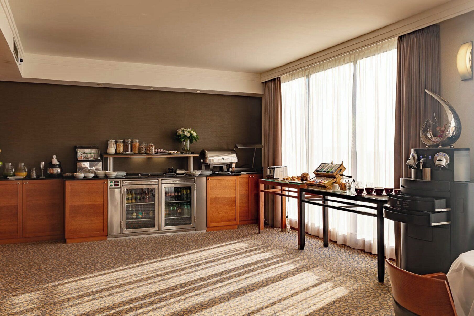 Habitación de hotel con kitchenette, zona de comedor y un ventanal grande con cortinas.