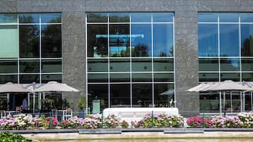 Een modern gebouw met grote ramen en terrasmeubels met parasols.