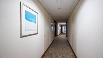 A hotel hallway with framed artwork on the walls, a patterned carpet, and doors leading to rooms.