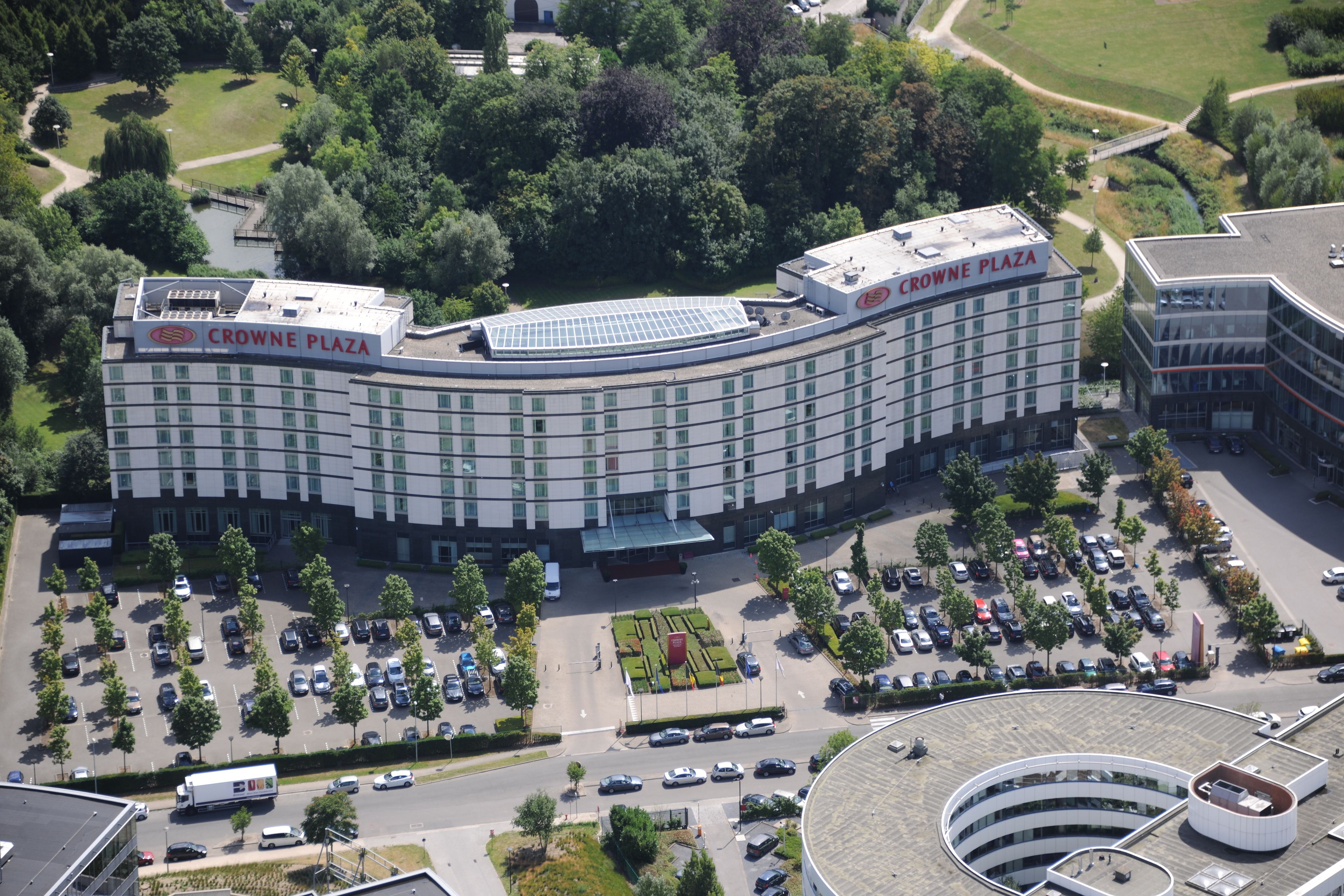 Ein großes, modernes Hotel mit gebogener Fassade, mehreren Etagen und einem Parkplatz mit einigen Autos.