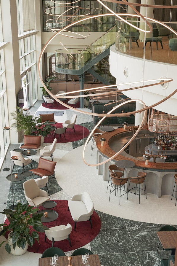 Un vestíbulo amplio con una zona de bar curva, espacios de asiento y una escalera que conduce a un nivel superior.