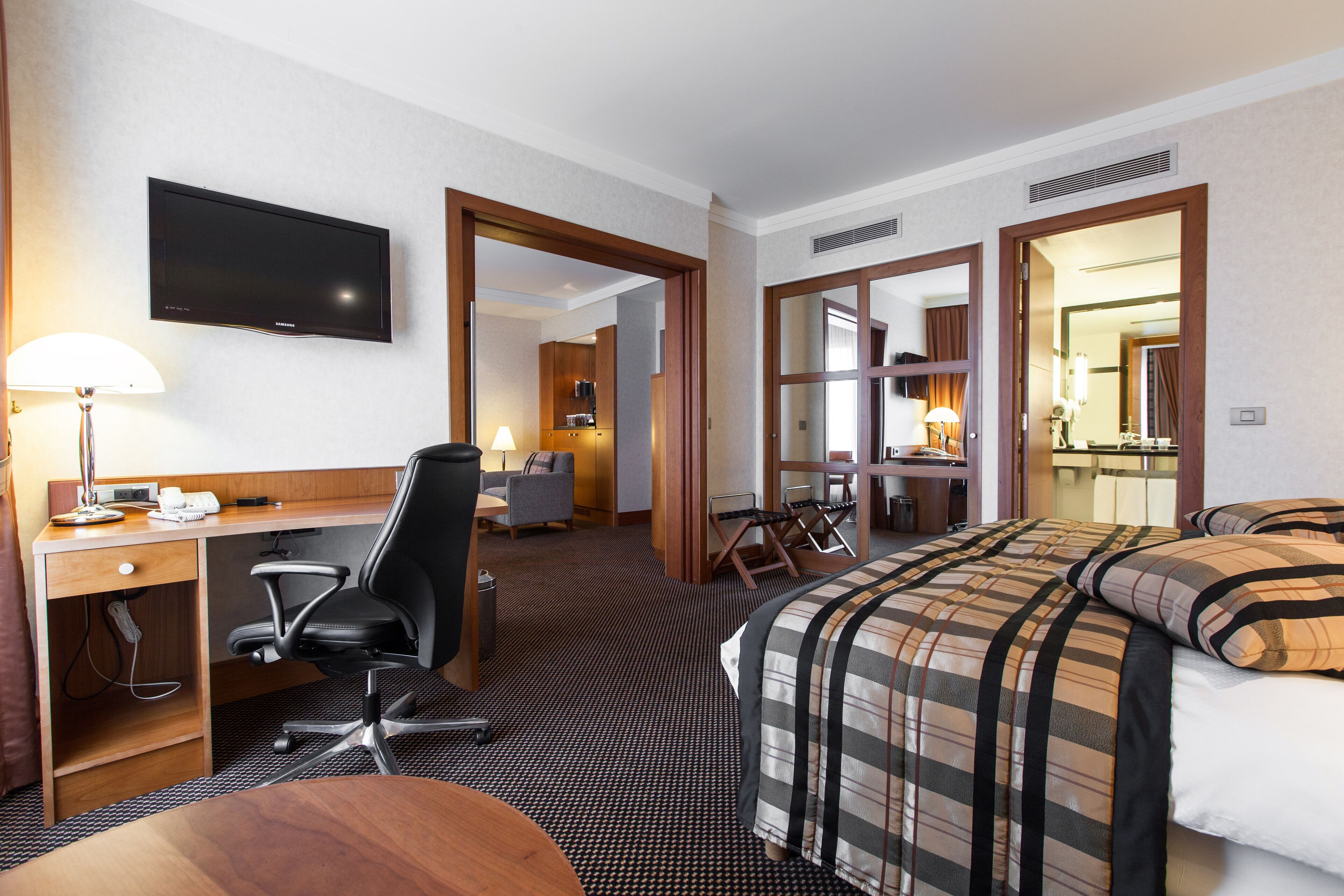 Une chambre d’hôtel avec un lit, un bureau, une chaise, une télévision et une salle de bain visible à travers une porte ouverte.