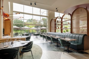 A restaurant with a modern interior, featuring a central seating area with a curved bench, surrounded by tables with chairs.