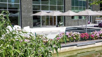 Un área de estar exterior moderna con sombrillas, una fuente de agua y un parterre de flores.