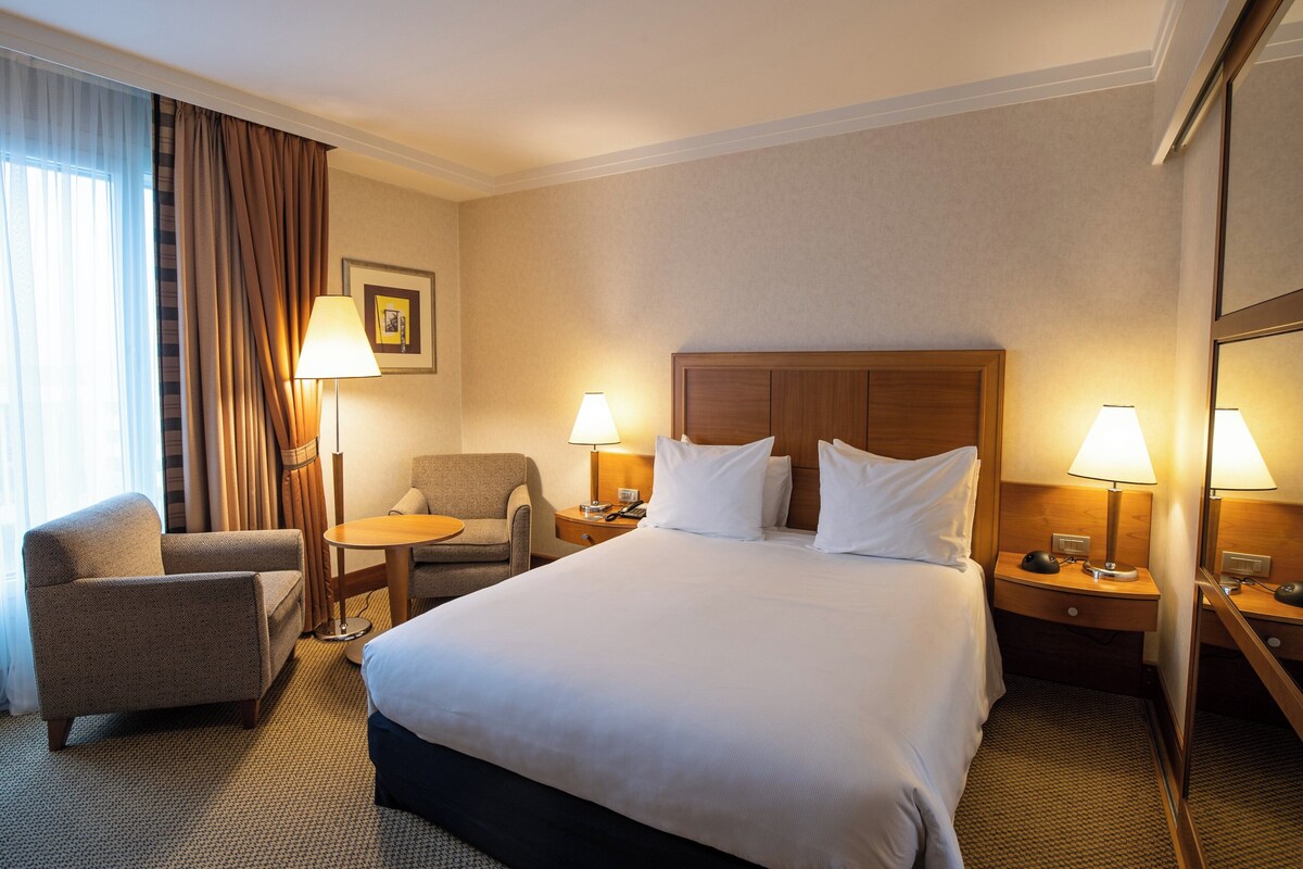 Ein Hotelzimmer mit einem großen Bett, zwei Nachttischen mit Lampen, einem Sessel und einem kleinen Tisch.