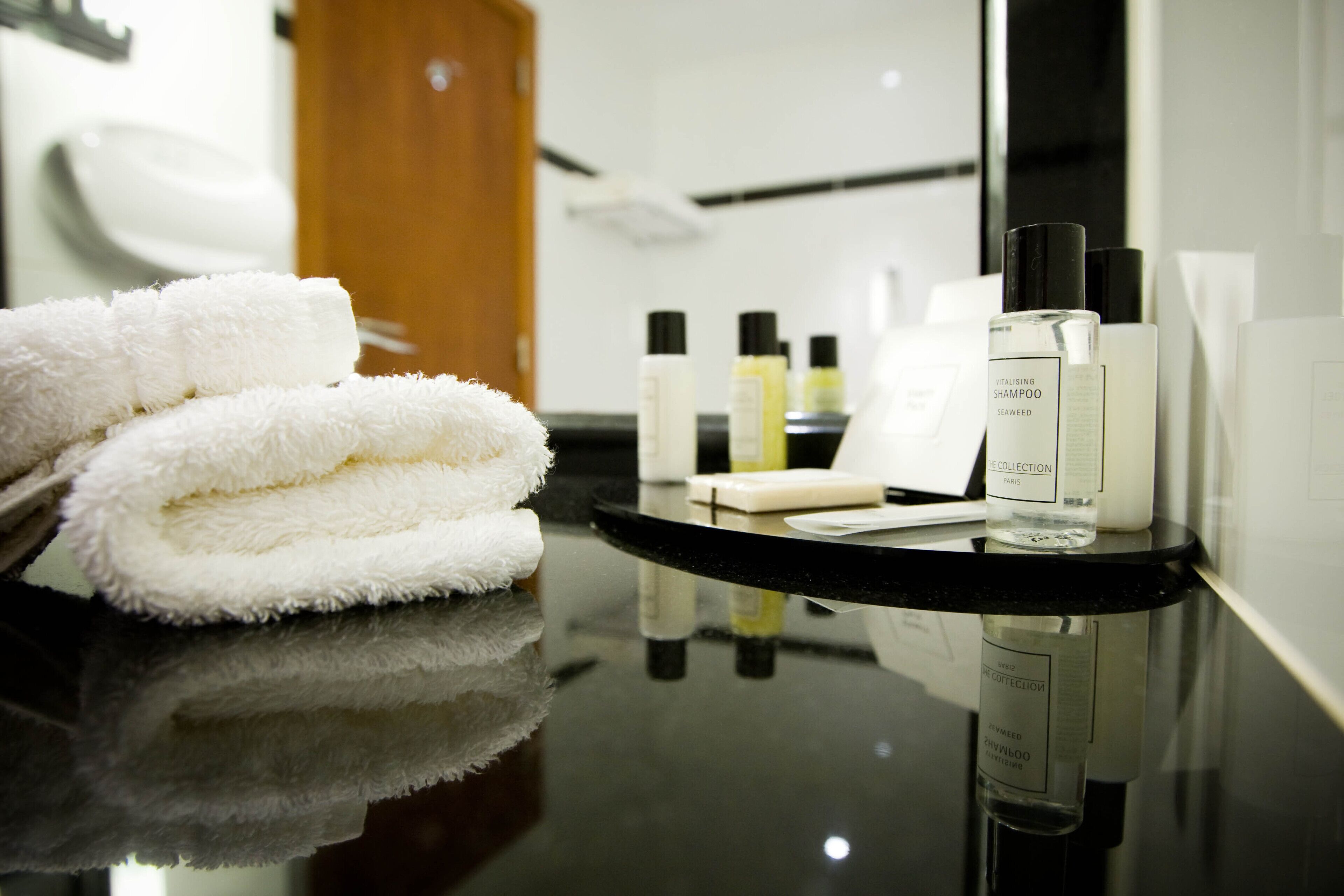 A bathroom with a black countertop, white towels, and various toiletries including a bottle labeled "Vitalising Shampoo Seaweed Collection."