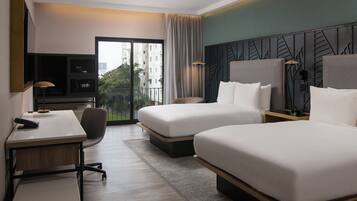 Habitación de hotel con dos camas, un escritorio, una silla, un televisor y vistas a edificios a través de la ventana.
