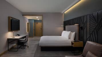A modern hotel room with a bed, desk, and seating area.