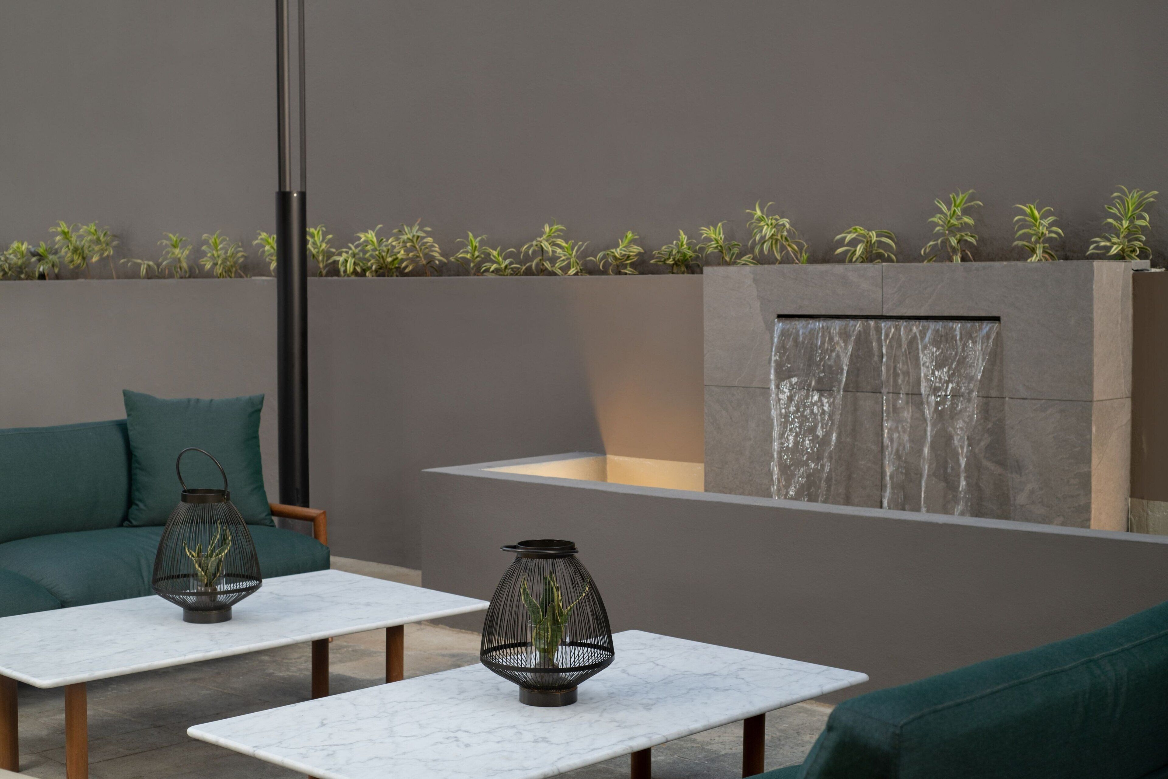 A modern outdoor seating area with two white marble tables, a green sofa, and a decorative wall with plants.