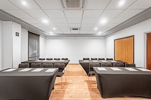 Un salón de conferencias con una mesa larga, sillas, una puerta de madera y una pared blanca.