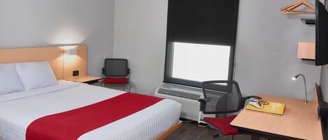 Habitación de hotel con cama, escritorio, silla y ventana con persiana negra.