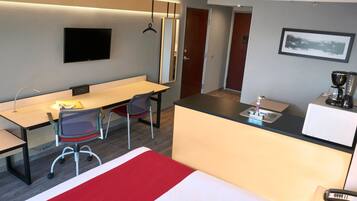Habitación de hotel con cama, escritorio, silla y kitchenette.