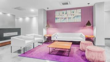 Un vestíbulo moderno con un sofá blanco, dos sillas blancas, una mesa de centro de madera y dos otomanas rosadas sobre una alfombra púrpura.