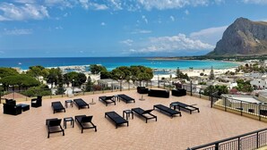 A rooftop terrace with sun loungers, a view of the sea, and a mountain in the background. - Hotel Panoramic (San Vito Lo Capo)