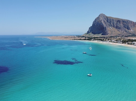 A coastal area with clear turquoise waters, boats, and a prominent rocky mountain.
