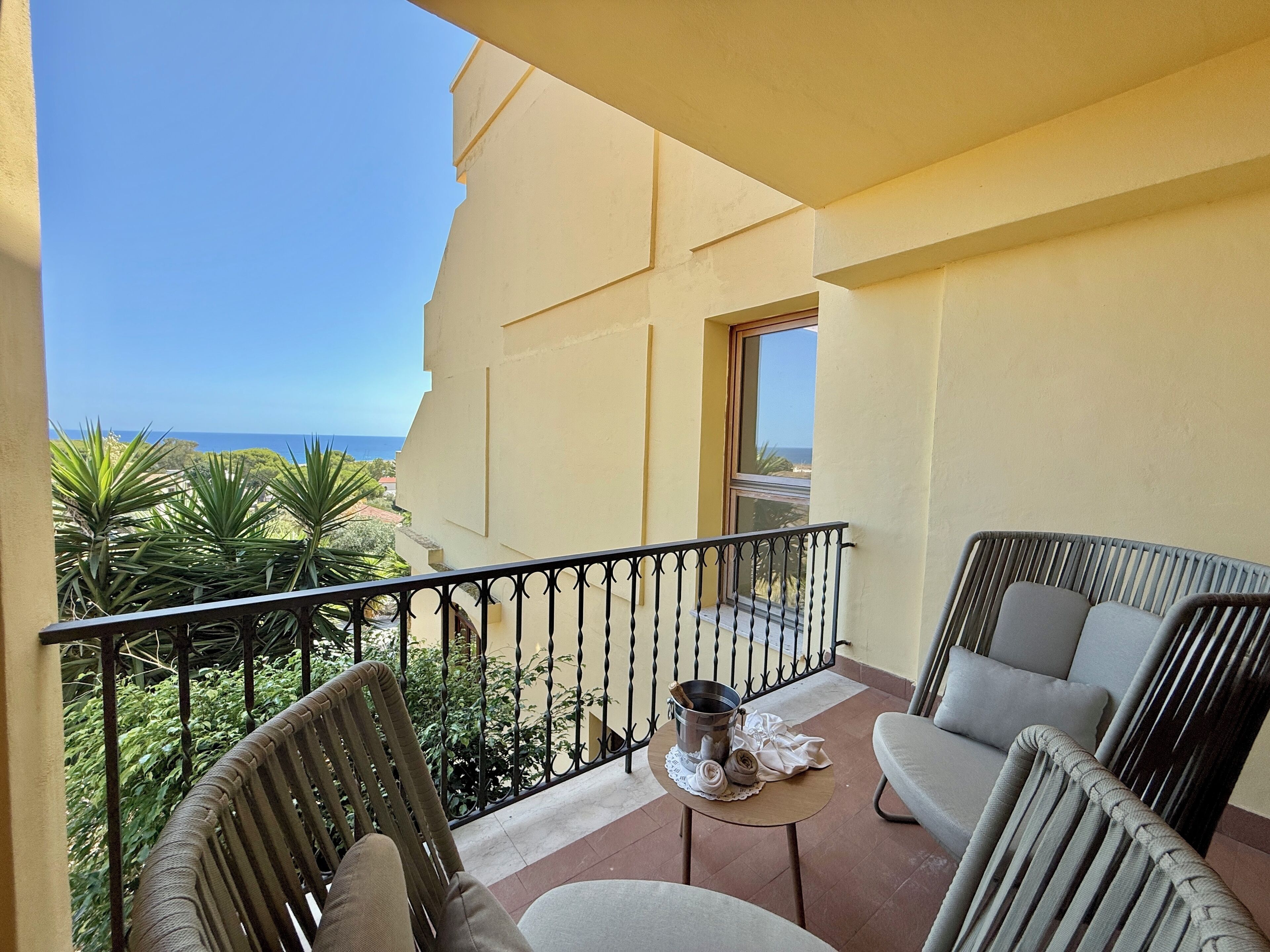 A balcony with wicker furniture, a small table with a metal bucket, and a view of the sea.