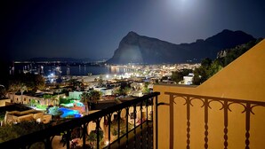 A night view of a coastal town with a prominent mountain in the background, a marina with boats, and a lit swimming pool area. - Hotel Panoramic (San Vito Lo Capo)