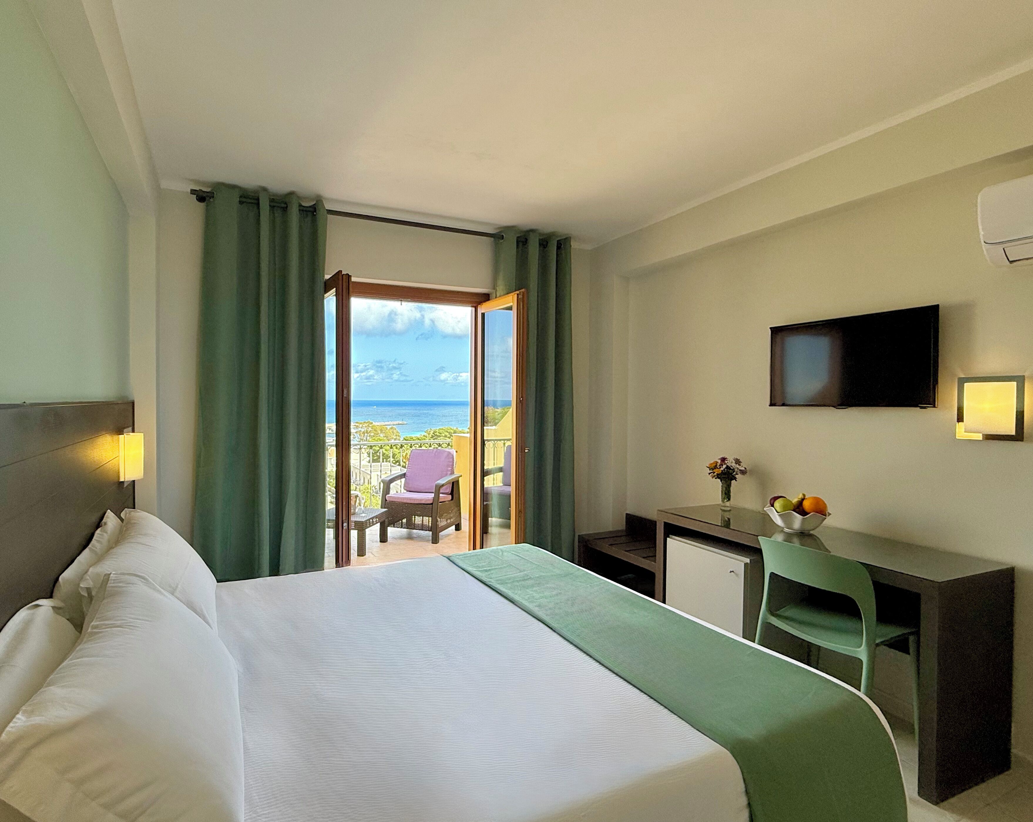 Habitación de hotel con cama, escritorio, silla, televisión y vista al océano.
