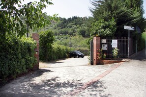 A gated entrance with a car parked inside, surrounded by greenery and a hill in the background.