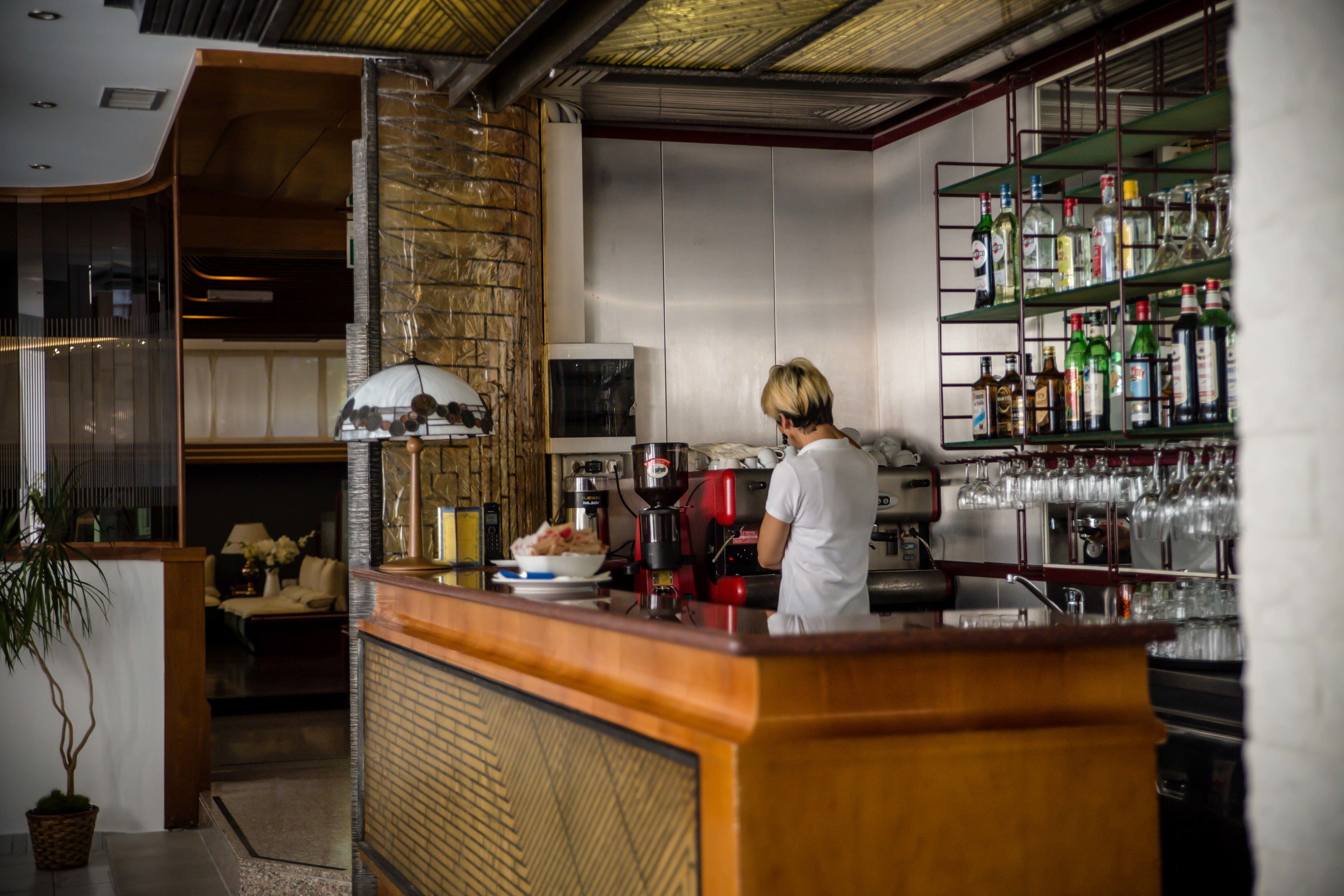 Una zona de bar con mostrador, estantes con botellas y una persona trabajando tras la barra.