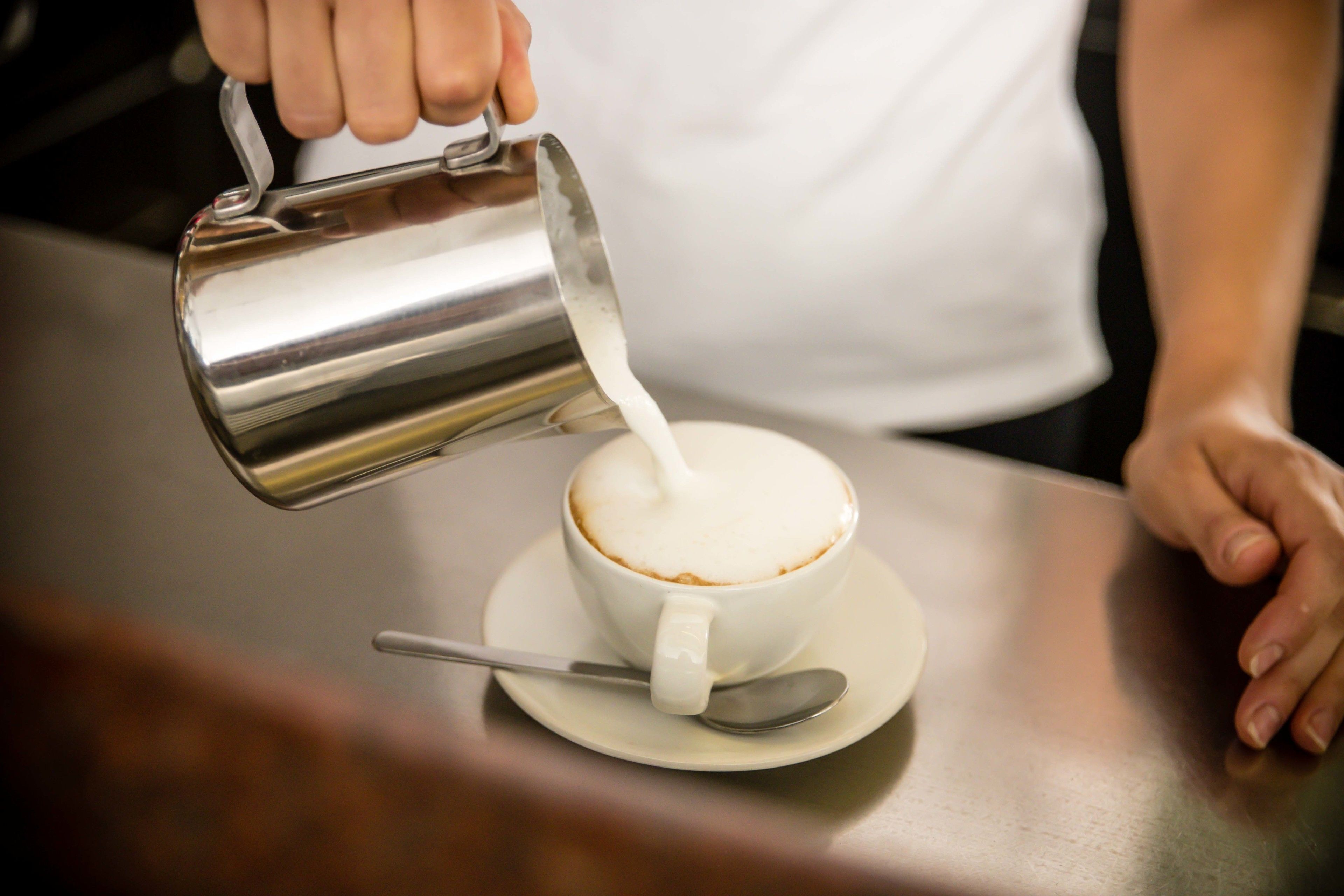 Algú abocant llet en una tassa de cafè.