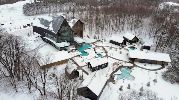 A modern lodge with multiple swimming pools, surrounded by snow-covered grounds and trees.