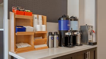 A kitchenette with a coffee maker, hot water dispenser, and storage for coffee cups and utensils.