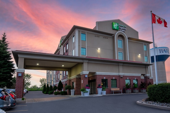 A Holiday Inn Express building with a red and white Canadian flag, a gas station sign, and a parking lot with cars. - Holiday Inn Express Hotel & Suites Barrie by IHG (Barrie)