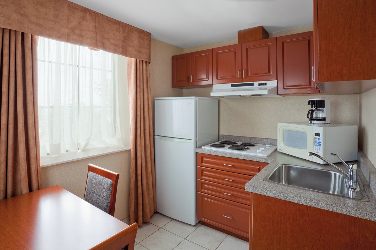 A compact kitchen with a refrigerator, microwave, stove, sink, and wooden cabinets.