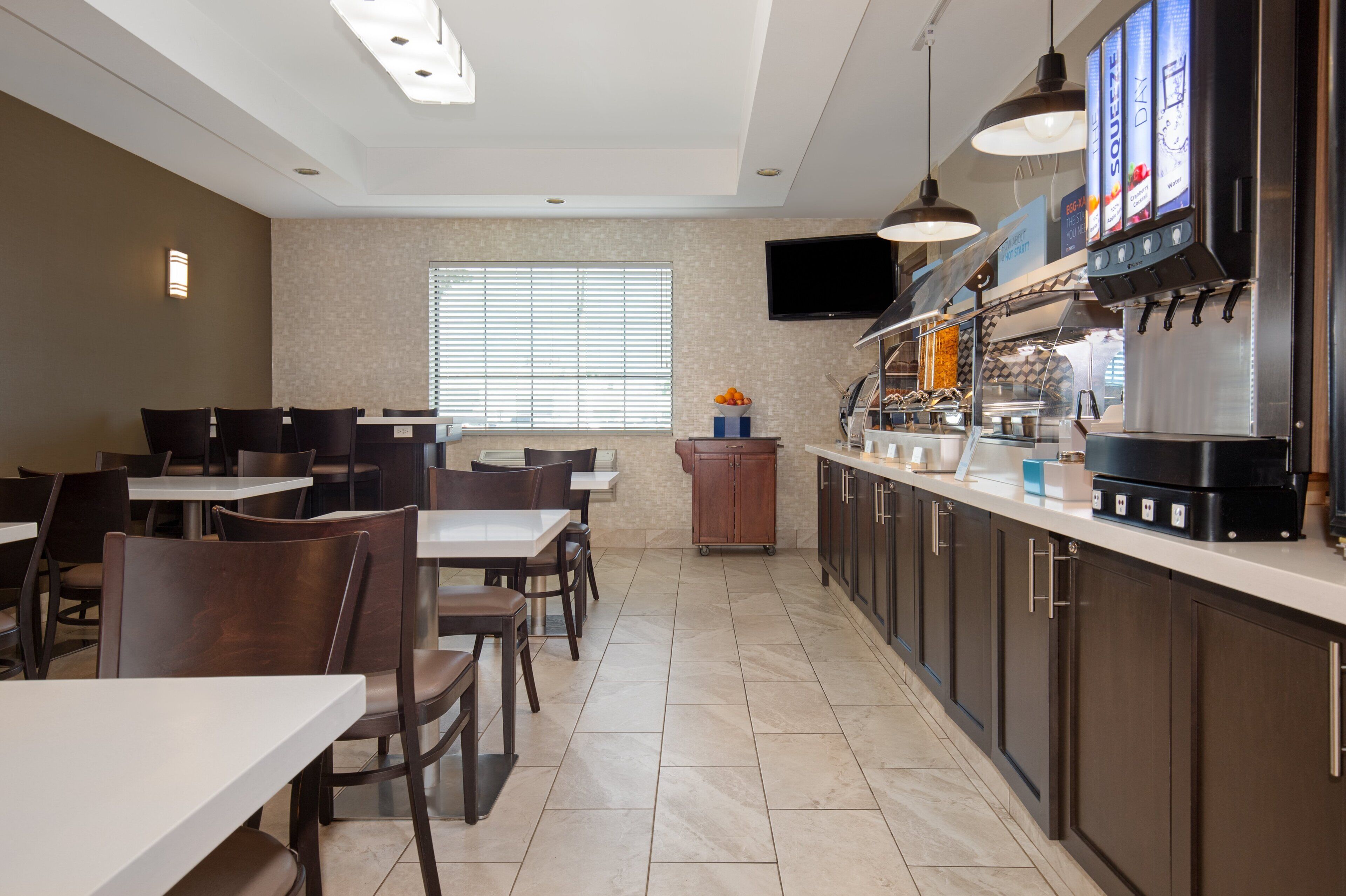 Un restaurant moderne doté d’un espace cuisine, de tables, de chaises et d’un téléviseur à écran plat fixé au mur.