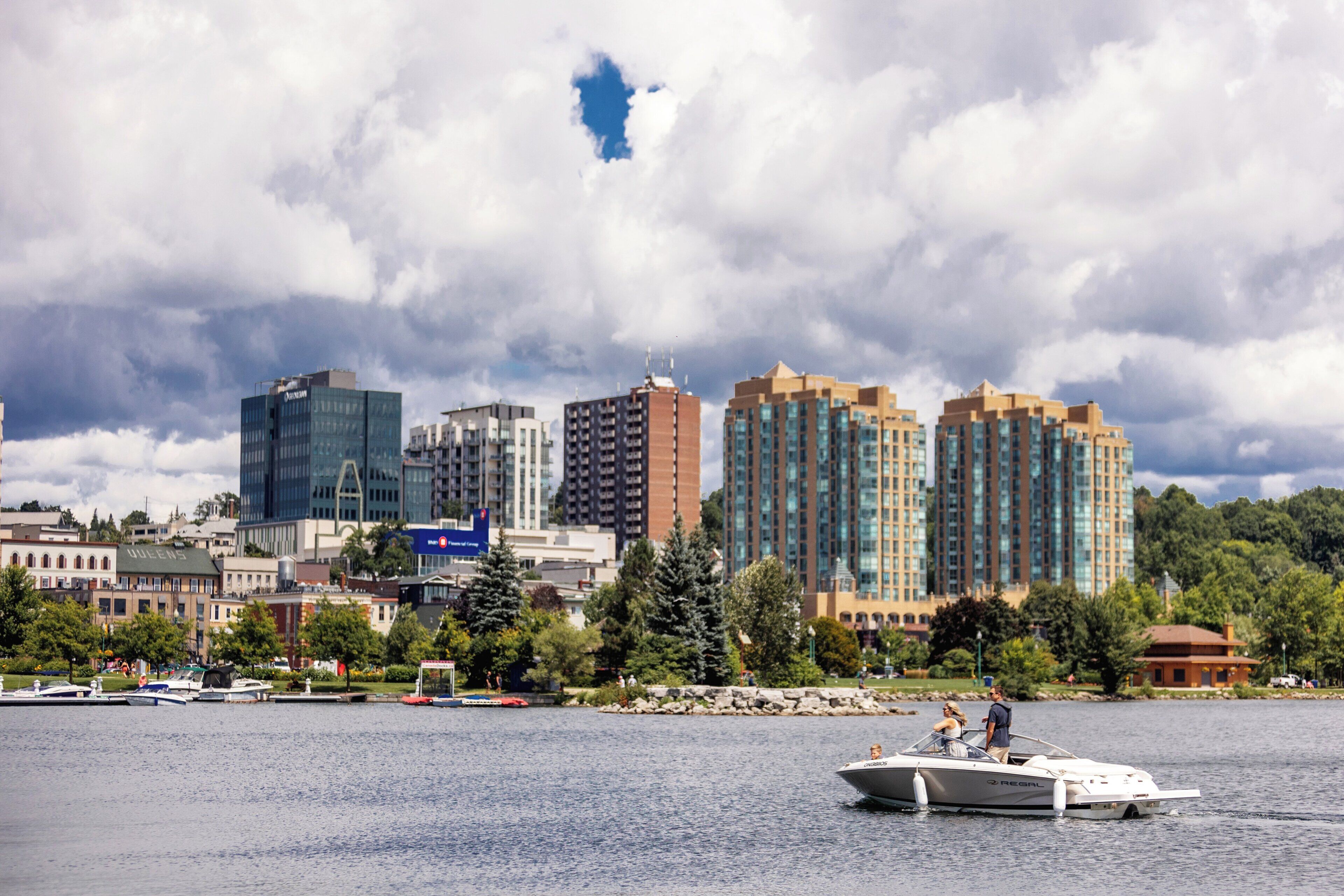 A waterfront cityscape with modern buildings, a marina with boats, and a clear sky.