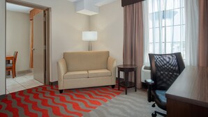 A hotel room with a sofa, a desk, a chair, a lamp, and a view of the outdoors through a window. - Holiday Inn Express Hotel & Suites Barrie by IHG (Barrie)