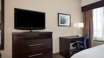 A hotel room with a flat-screen TV, a desk with a chair, a bed, and a framed picture on the wall.