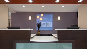 A reception area with a Holiday Inn Express sign, a vase with a plant, and a reception desk with a computer.