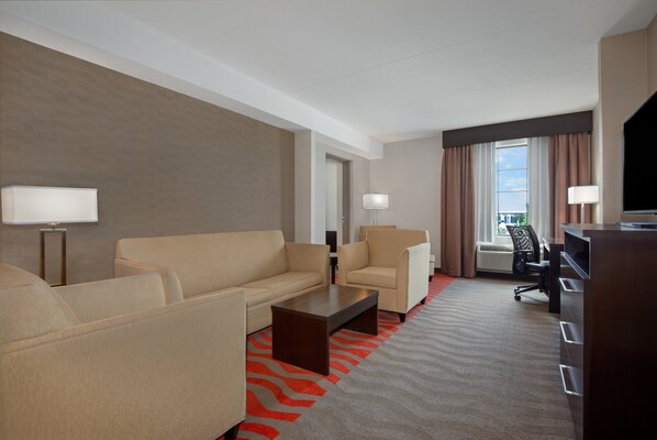 A hotel room with a beige sofa, two armchairs, a wooden coffee table, a desk, and a TV. - Holiday Inn Express Hotel & Suites Barrie by IHG (Barrie)
