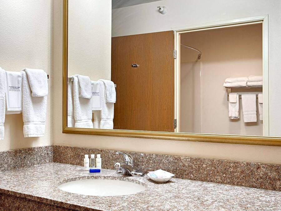 Un baño con encimera de granito, lavamanos, espejo y puerta de madera.