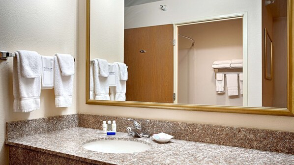 A bathroom with a granite countertop, a sink, a mirror, and a wooden door. - Best Western J. C. Inn (Junction City)