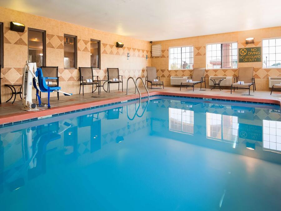 En swimmingpool med liggestole og solsenge, en flisevæg med geometriske mønstre, samt et skilt der angiver, at dykning ikke er tilladt, og der ikke er livredder på vagt.