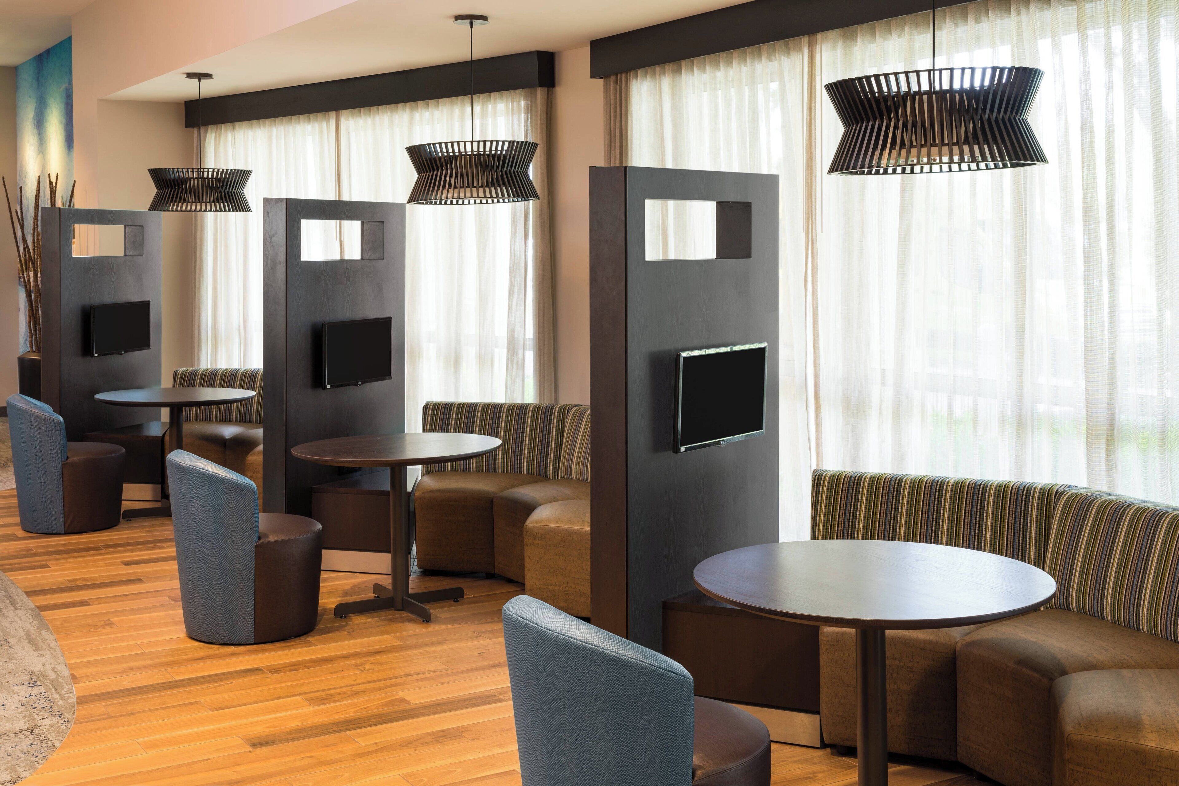 Un espacio lounge moderno con sofás, sillones y mesas, que cuenta con un televisor de pantalla plana e iluminación colgante.