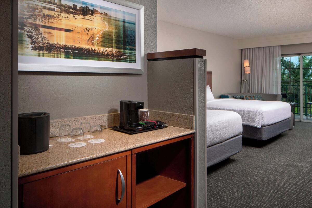 A hotel room with a bed, a coffee maker, a framed picture on the wall, and a window with curtains.