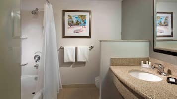 A bathroom with a bathtub, a sink, a toilet, and a shower curtain. There are towels hanging on the wall and a framed picture above the sink.